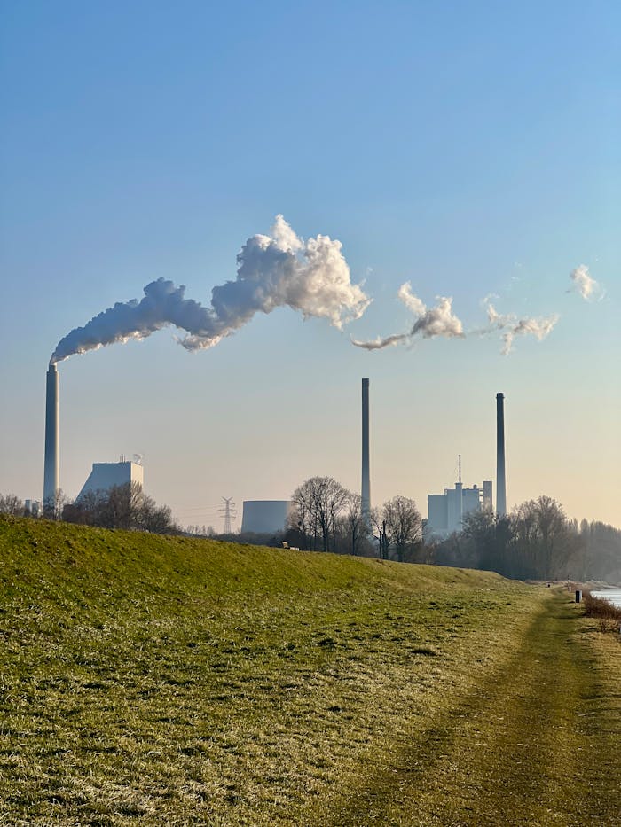 Industrial chimneys with smoke emissions under a clear blue sky in a rural setting.